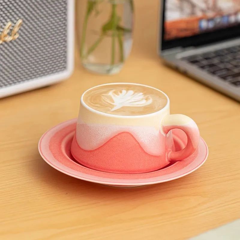 Koralowa filiżanka Sento ze spodkiem i kawą z latte art na biurku