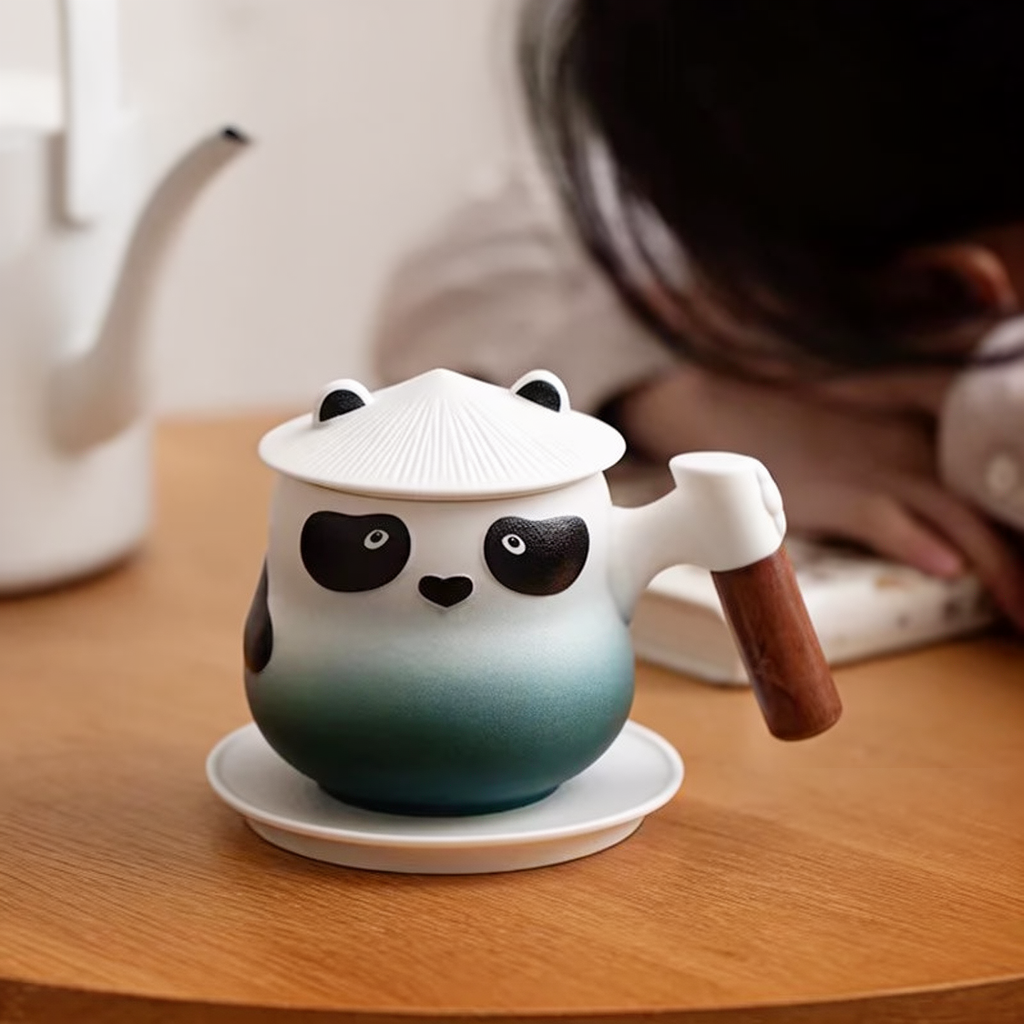 Ciemnozielono-biały kubek Panda z jasną pokrywką i spodkiem na stole