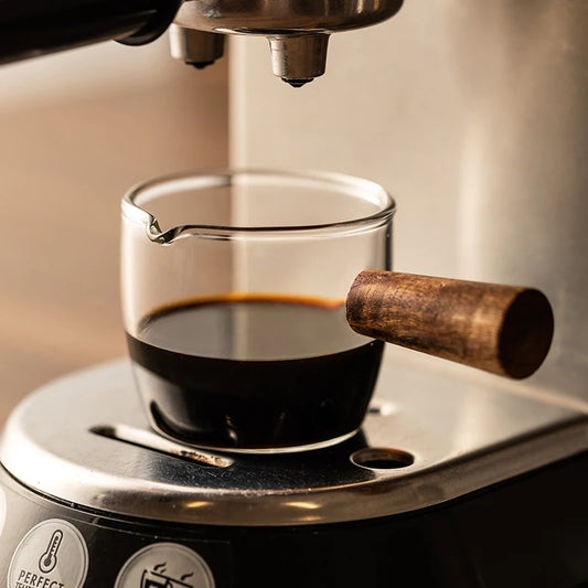 Szklana miarka z drewnianym uchwytem wypełniona espresso pod kolbą ekspresu